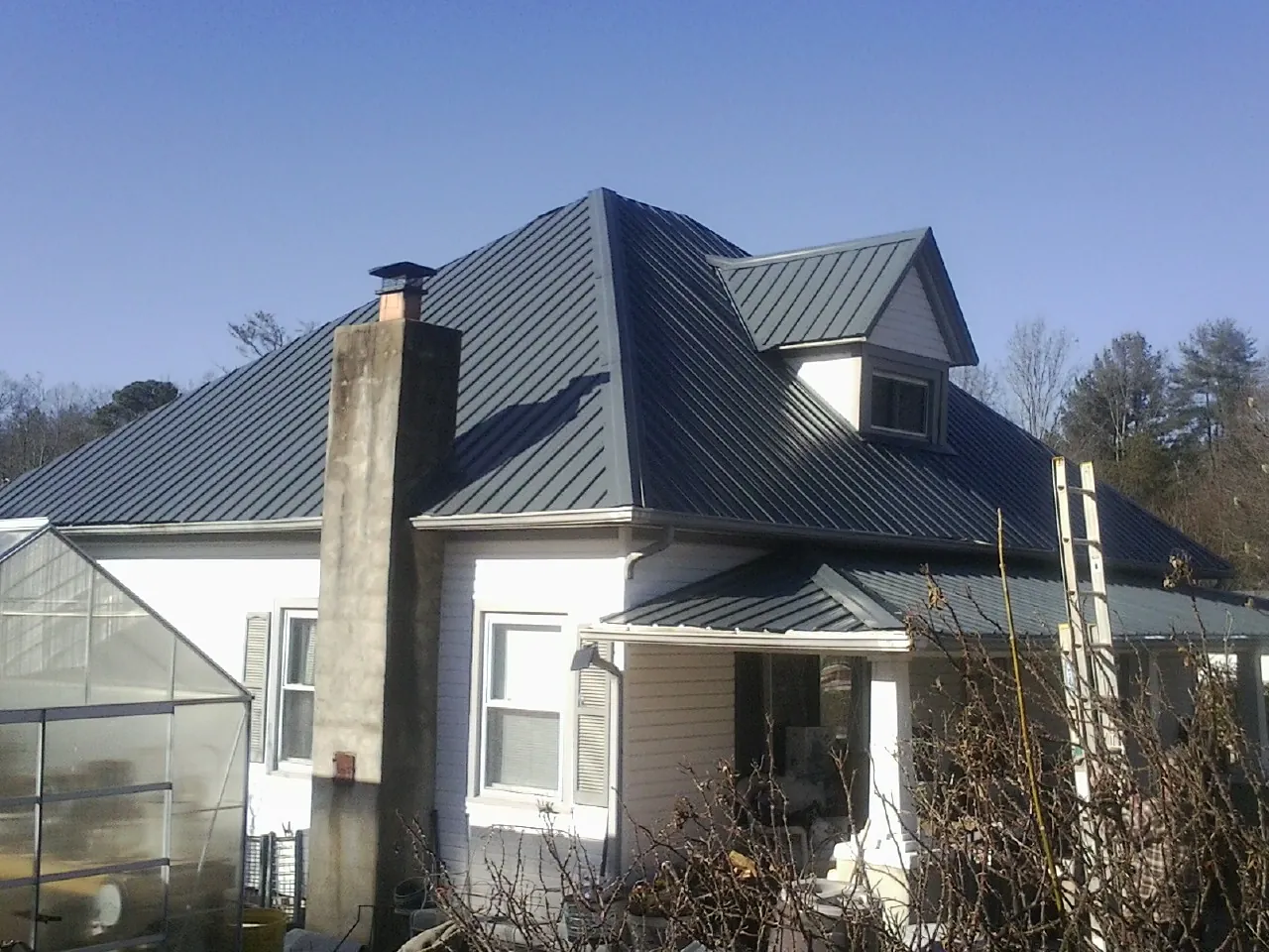 Dark blue standing seam metal roof on a white farmhouse with dormer — Slate & Tile Roof Repair by Roofing Brothers in South Heart