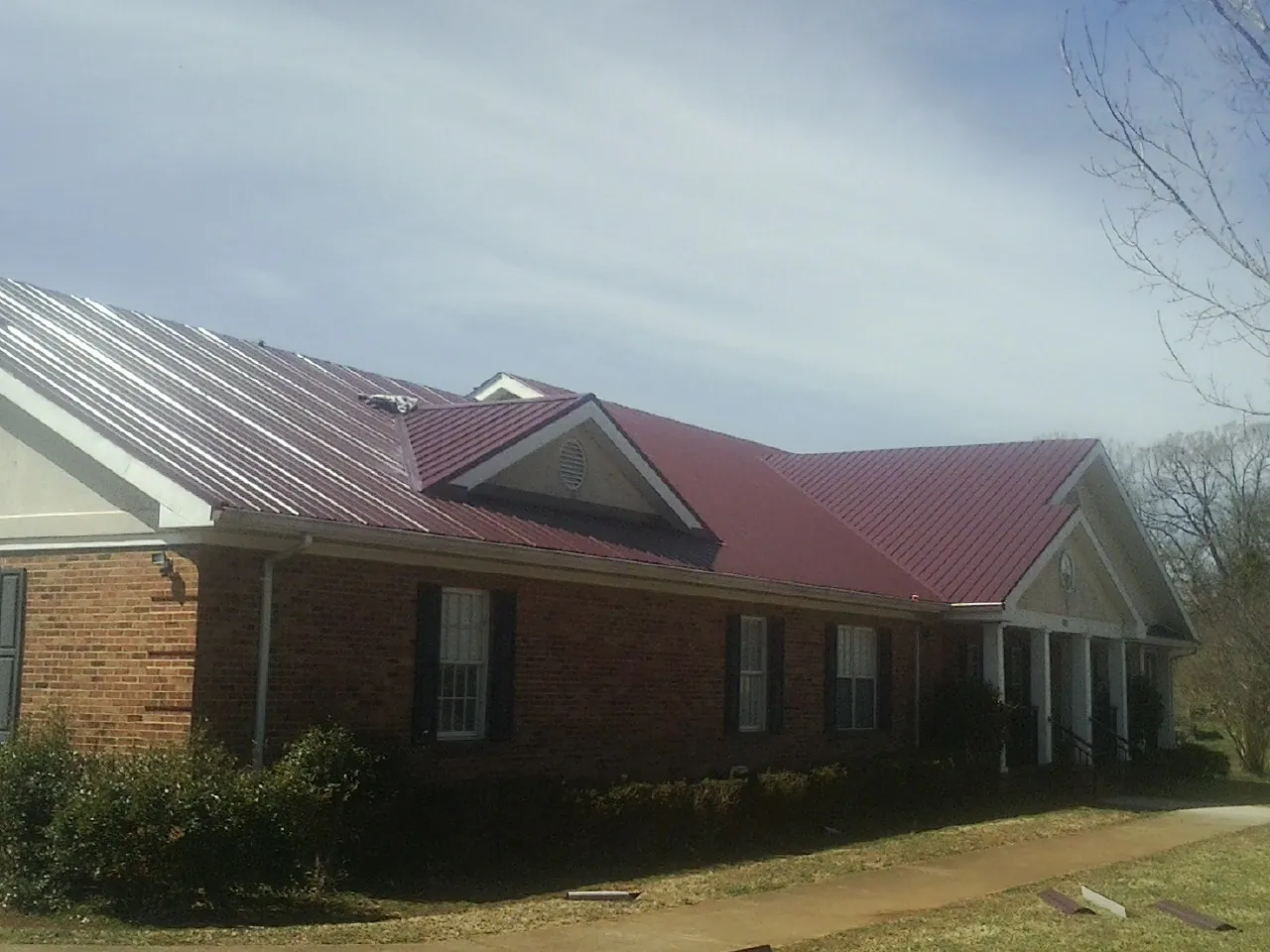 Red metal roof with gabled entries on a long brick building, from a Hail Damage Roof Repair job in South Heart