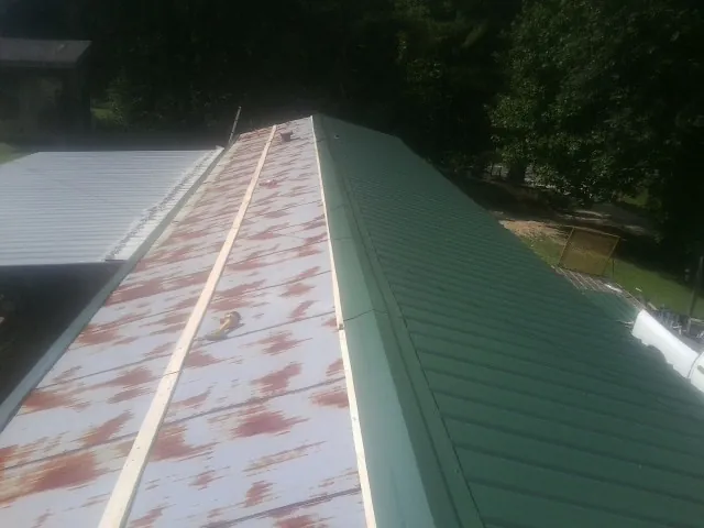Old rusted panels beside newly installed green metal roofing — Wind Damage Roof Repair by Roofing Brothers in South Heart