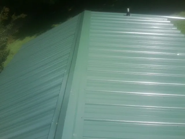 New green metal panels meeting at the ridge of a roof — Flat Roof Repair work by our crew in South Heart