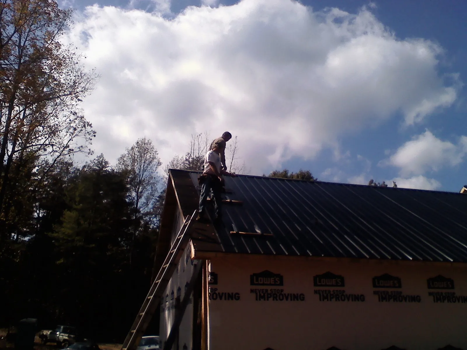 Roofer fastening dark metal panels high against a cloudy sky, from a Roof Inspection job in South Heart