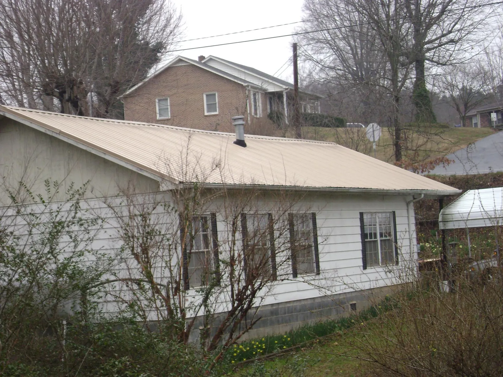 Tan metal roof on a white sided house set into a hillside — Commercial Roofing by Roofing Brothers in South Heart